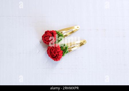 Rote Blume gestrickt mit Häkeln, als Haarspangen, auf einem alten weißen Holztisch Stockfoto