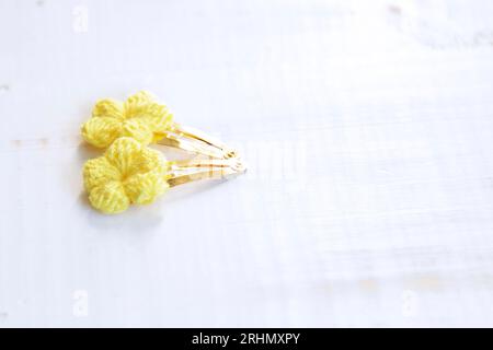 Gelbe Blumen, gestrickt mit Häkeln, als Haarspangen, auf einem alten weißen Holztisch Stockfoto