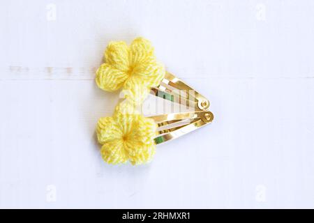 Gelbe Blumen, gestrickt mit Häkeln, als Haarspangen, auf einem alten weißen Holztisch Stockfoto