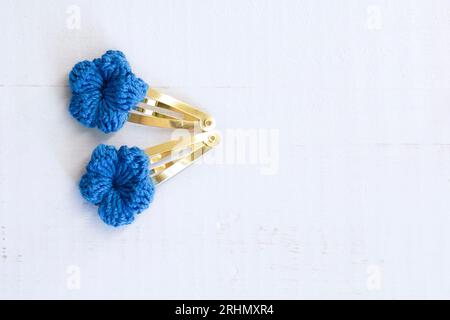 Blaue Blumen mit Häkelarbeit, als Haarspangen, auf einem alten weißen Holztisch mit Kopierraum. Stockfoto
