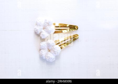Weiße Blumen, die mit Häkeln gestrickt wurden, als Haarspangen, auf einem alten weißen Holztisch Stockfoto