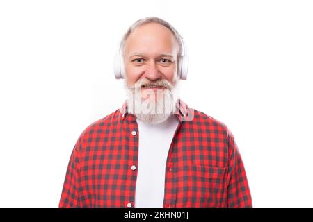 Ein 60-jähriger, grauhaariger Rentner mit Bart und Schnurrbart im Hemd hört Musik über Kopfhörer ohne Kabel Stockfoto