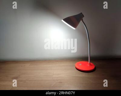 Eine moderne rote Schreibtischlampe mit weißem geschwungenem Hals, die mit Akkus betrieben wird, strahlt weiches LED-Licht auf eine Holzoberfläche aus. Stockfoto