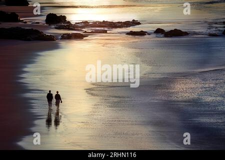 Ein Paar mittleren Alters, das am Abend barfuß am Strand spaziert Stockfoto