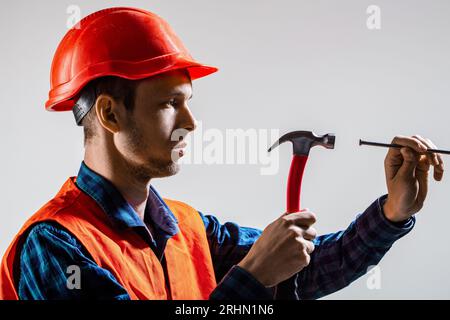 Man-Builder. Hammerschlag. Baumeister in Helm, Hammer, Handwerker, Baumeister in Schutzhelm. Hammerhandnagel. Die Hände des Mannes halten einen Hammer und eine Nagelung Stockfoto