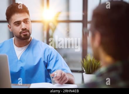 Amerikanischer Arzt, der mit einem Patienten spricht, während er im Büro sitzt Stockfoto