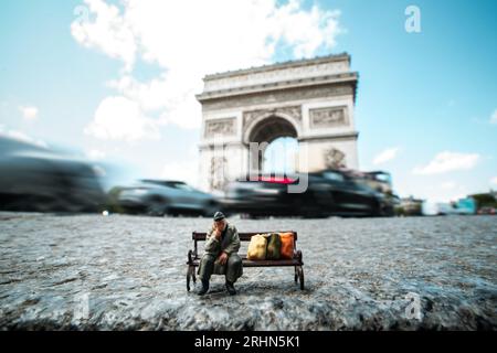 Miniatur-Obdachloser sitzt auf einer Bank vor dem Arc de Triomphe in Paris, Frankreich Stockfoto