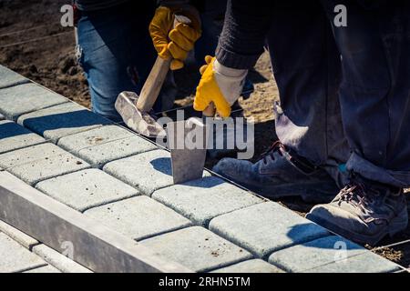 Männliche Hand mit Maurerhammer, die den Bürgersteig repariert Stockfoto