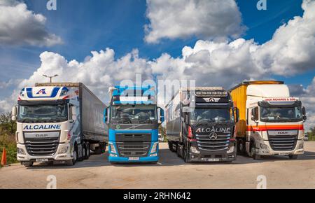 Vier kommerzielle knickgelenkte Lastkraftwagen oder Lkw mit einer Tragfähigkeit von jeweils bis zu 44 Tonnen, die in einer Linie am Lincoln Farm Truck Stop in Balsall geparkt sind Stockfoto