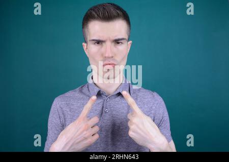 Überselbstbewusster junger gutaussehender Kaukasier in grauem T-Shirt-Mann zeigt sich mit arrogantem Ausdruck auf isoliertem Hintergrund Stockfoto