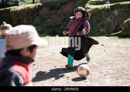 Peruanisches Mädchen mit farbenfroher Kleidung, das Fußball spielt Stockfoto