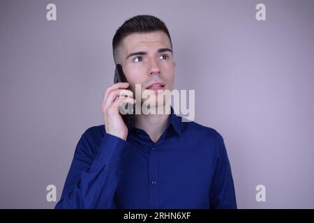 Eleganter junger gutaussehender kaukasischer Mann, der am Telefon auf isoliertem Hintergrund spricht Stockfoto