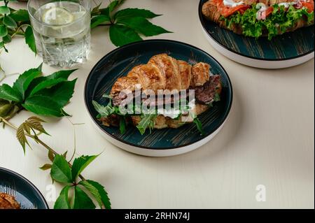 Croissant mit Frischkäse, gegrilltem Rindfleisch, Gemüse und Kräutern. Stockfoto