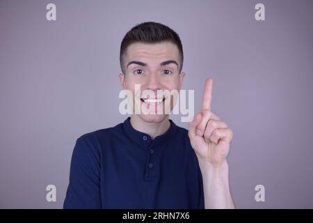 Lächelnder junger gutaussehender Kaukasier zeigt mit brillanter Ideengeste auf isoliertem Hintergrund Stockfoto