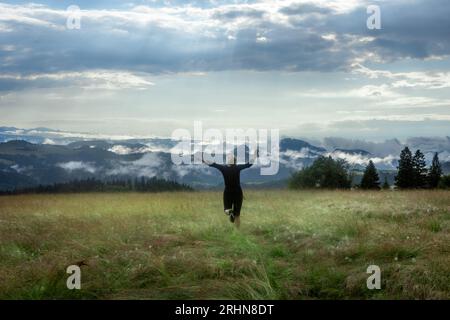 Jaworki, Polen - 19. Juli 2023: Eine Frau in Schwarz, die auf eine Berglandschaft in Beskid Sadecki, Polen, zuläuft. Nebel steigt nach Regen aus Tälern auf. Stockfoto