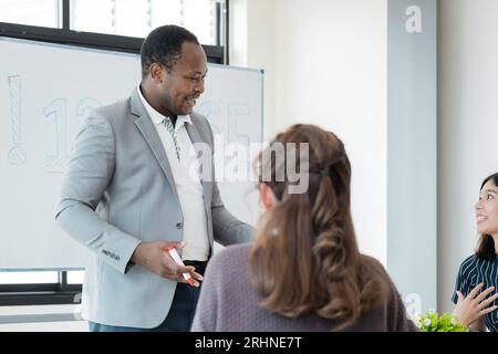Positiv freundlicher Afro-amerikanischer Englischlehrer, der einer Gruppe von Schülern verschiedener Nationalitäten Sprachkurse anbietet, die am Tisch sitzen Stockfoto