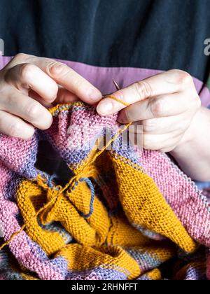 Vorderansicht des Strickpullovers für weibliche Hände aus Wollgarn auf Stahlstricknadeln aus der Nähe Stockfoto
