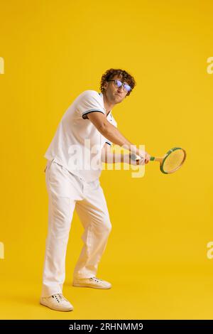 Reifer Mann in Brille und weißer Kleidung mit Tennisschläger, Training, Spiel vor gelbem Studiohintergrund Stockfoto