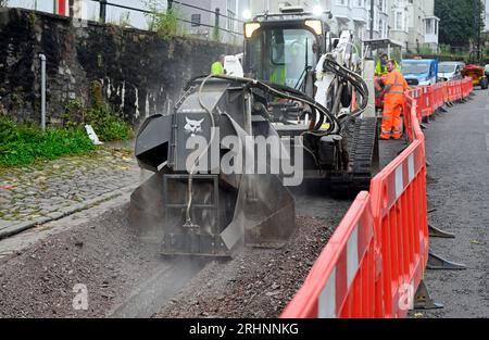 Grabenfräse (Bobcat) zum Schneiden von Kanälen durch Pflaster in der Straße zum Verlegen von Entenarbeit für Glasfaserkabel, Großbritannien Stockfoto