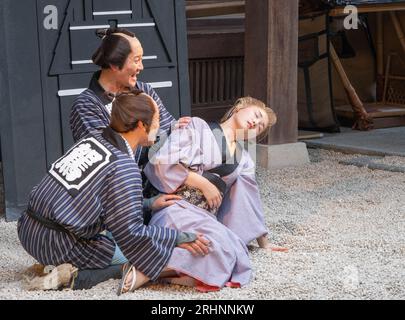 Zwei Männer in historischen Kostümen, die eine tote Frau in Yukata in einem Comedy-Stück aus der edo-Zeit im edomura Wonderland tragen. Stockfoto