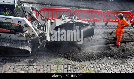 Grabenfräse (Bobcat) zum Schneiden von Kanälen durch Pflaster in der Straße zum Verlegen von Entenarbeit für Glasfaserkabel, Großbritannien Stockfoto