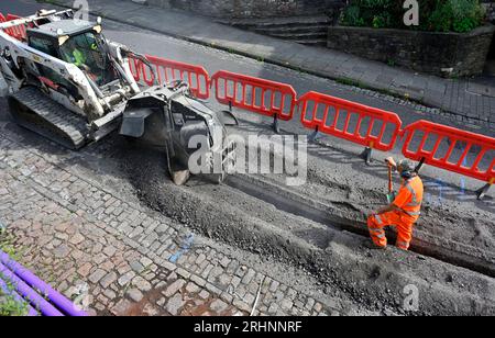 Grabenfräse (Bobcat) zum Schneiden von Kanälen durch Pflaster in der Straße zum Verlegen von Entenarbeit für Glasfaserkabel, Großbritannien Stockfoto