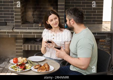Ein Paar mittleren Alters isst im Hinterhof Fleisch und Wein Stockfoto