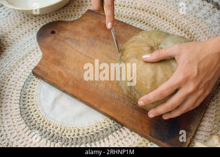 Draufsicht auf unerkennbare kaukasische weibliche Hände, die Kürbis auf einem hölzernen Schneidebrett zuschneiden, um vegetarisches Essen zuzubereiten Stockfoto