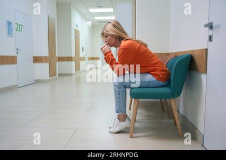 Frustrierte Frau sitzt in einem Krankenhauskorridor, der Raum ist hell und sauber Stockfoto
