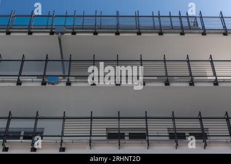 Blick von unten auf die Fassade eines modernen Gebäudes mit Balkonen und Stahlgeländern und einem klaren blauen Himmel Stockfoto