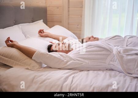 Glückliches Paar in Bademänteln, die auf dem Bett liegen Stockfoto