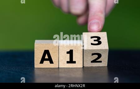 Symbol für eine Lohnerhöhung in Deutschland. Hand dreht Holzwürfel und ändert die deutsche Gehaltsstufe von A12 auf A13. Stockfoto