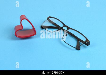 Lesebrille mit Herz an der Seite. Konzept der Bequemlichkeit der Brille isoliert auf blauem Hintergrund. Foto mit hoher Auflösung. Volle Tiefe o Stockfoto