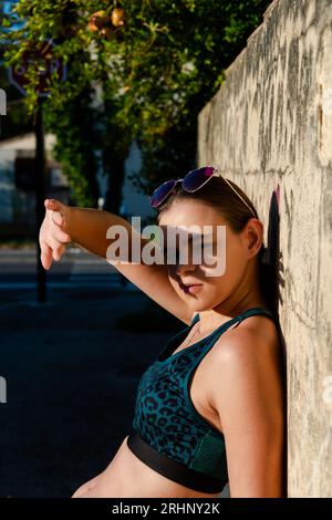 Schöne Frau, die ihre Hand über ihren Augen hält, das Gesicht vor den Sonnenstrahlen schützt. Sie lehnt sich an die Wand, Schutzkonzept, Hautkrebs, Hautauto Stockfoto