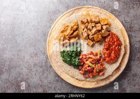 Äthiopische Injera mit Fleisch, Gemüse und Grünzeug aus nächster Nähe auf dem Holzbrett auf dem Tisch. Horizontale Draufsicht von oben Stockfoto