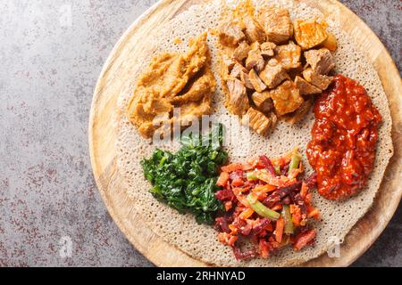 Äthiopisches Injera Fladenbrot mit verschiedenen Gemüse- und Fleischfüllungen aus nächster Nähe auf dem Holzbrett auf dem Tisch. Horizontale Draufsicht von oben Stockfoto