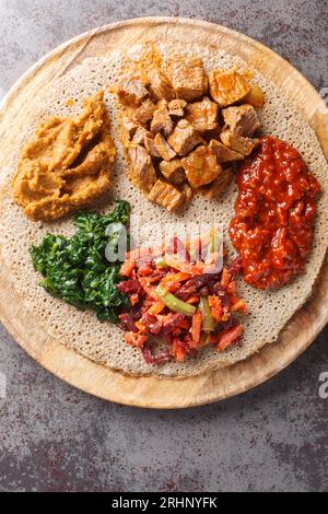 Mischen Sie Gemüse und Eintöpfe auf injera Fladenbrot aus nächster Nähe auf dem Holzbrett auf dem Tisch. Vertikale Draufsicht von oben Stockfoto