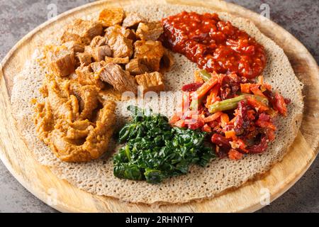 Äthiopisches Injera Fladenbrot mit verschiedenen Gemüse- und Fleischfüllungen aus nächster Nähe auf dem Holzbrett auf dem Tisch. Horizontal Stockfoto