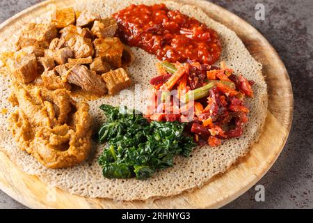 Äthiopische Injera mit Fleisch, Gemüse und Grünzeug aus nächster Nähe auf dem Holzbrett auf dem Tisch. Horizontal Stockfoto