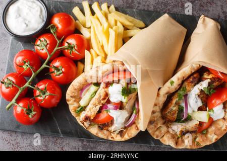 Griechischer Fast Food Gyros mit Huhn, Tomaten, Gurken und Zwiebeln serviert mit Tzatziki-Sauce und Pommes Frites aus nächster Nähe auf einem Brett auf dem Tisch. Horiz Stockfoto