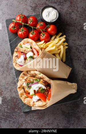 Griechische Gyros mit Huhn und frischem Gemüse, serviert mit Tzatziki-Sauce und Pommes Frites aus nächster Nähe auf einem Brett auf dem Tisch. Vertikale Draufsicht von abo Stockfoto