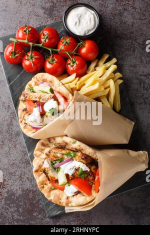 Leckeres griechisches Hühnchen-Gyros mit Gemüse, Pommes frites und Tzatziki-Sauce auf dem Tisch. Vertikale Draufsicht von oben Stockfoto