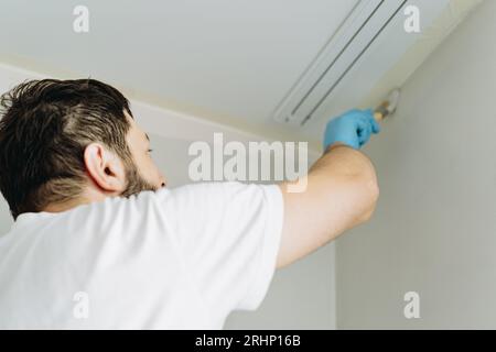kaukasischer bärtiger Mann malte Wand mit Pinsel. Malerwohnung, renovierendes Haus mit grauer Farbe. Bild mit selektivem Fokus Stockfoto