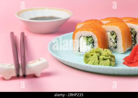 Sushi rollt Philadelphia mit Lachs und Avocado. Rolle fertig zum Essen auf blauem Teller mit Wasabi und Sojasauce. Asiatische oder japanische Küche, orientalische Küche. Stockfoto