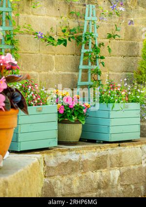 Im Sommer gibt es in einem Terrassengarten hölzerne Pflanzgefäße mit Topfpflanzen wie Lobelien, Ringelblumen und Petunien. Stockfoto