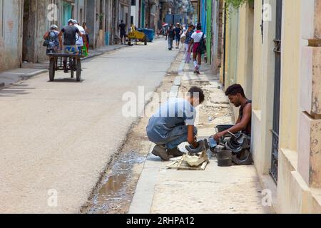 Havanna, Kuba - 27. Juli 2023: Zwei junge kubanische Männer arbeiten auf dem Bürgersteig. Stadtleben im Hintergrund Stockfoto