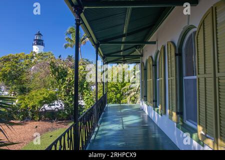 Key West, Florida, USA. Blick auf die obere Veranda des Ernest Hemingway Home and Museum, Altstadt, historischer Leuchtturm, der über Bäumen zu sehen ist. Stockfoto