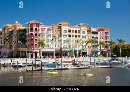 Neapel, Florida, USA. Blick über den Gordon River auf die farbenfrohe Architektur des Bayfront Place, Kajakfahrer überqueren den Yachthafen. Stockfoto