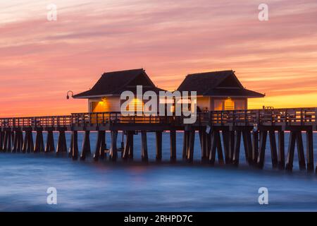 Neapel, Florida, USA. Beleuchtete Holzhütten am Naples Pier, Abenddämmerung, spektakulärer rosa Himmel über dem Golf von Mexiko. Stockfoto