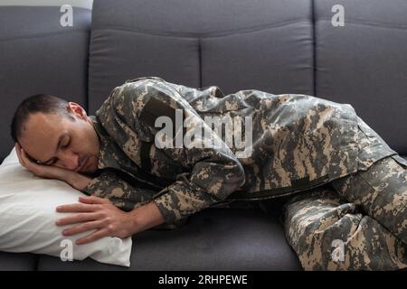 Verschwommener Junge, der erschöpften Vater in Tarnung ansieht und auf der Couch im Wohnzimmer mit weihnachtsdekoration schläft Stockfoto